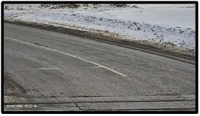 LPR camera view of an empty snow-lined road approaching a railway crossing