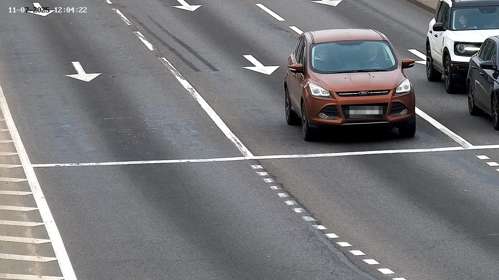 LPR camera view of an orange SUV crossing lane-direction arrows on a multi-lane road with other vehicles alongside