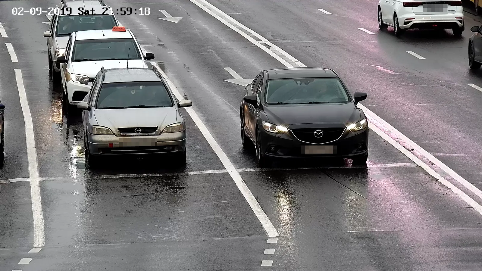 LPR camera view of a sedan and other vehicles queued in a lane on a wet multi-lane road