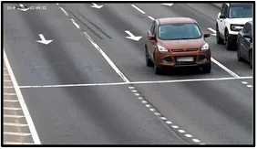 Entry LPR camera view of a crossover vehicle approaching the intersection with lane-direction arrows painted on the road
