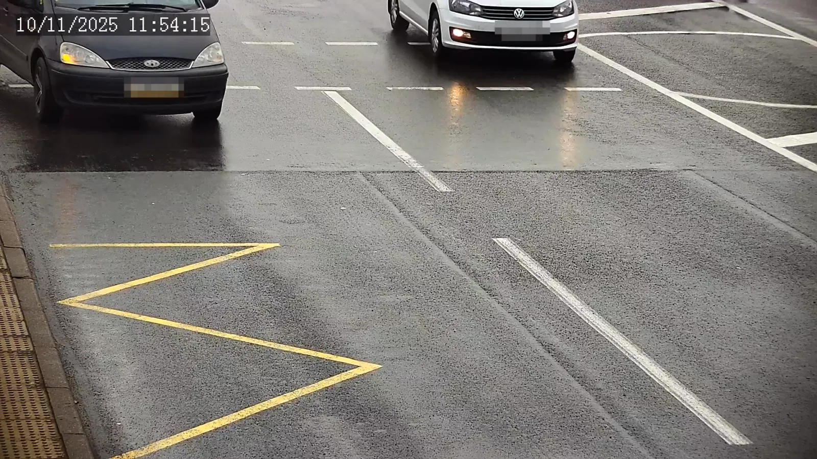 LPR camera view of two vehicles crossing an intersection stop line marked with a yellow zigzag no-stopping marking