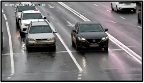 Entry LPR camera view of two sedans approaching the intersection stop line on a wet road with a timestamp overlay