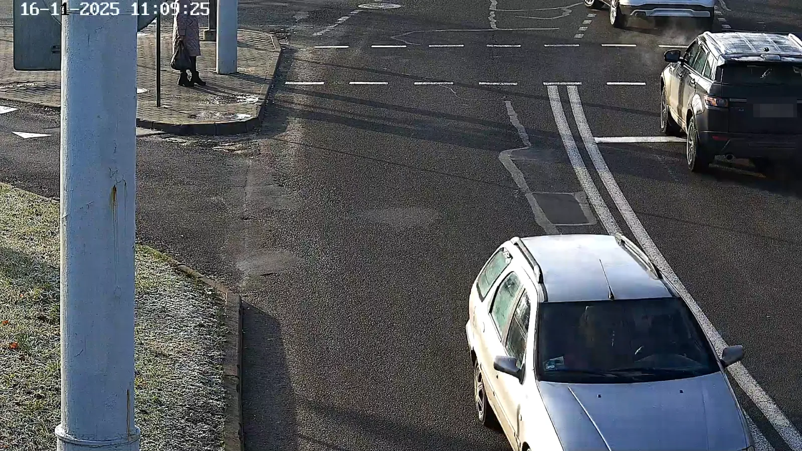 LPR camera view of an intersection with a pedestrian waiting at a bus shelter and vehicles crossing in the background