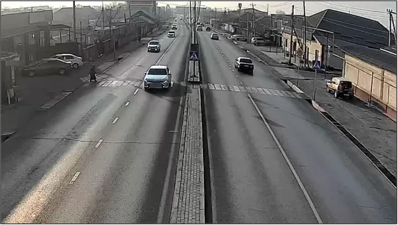 OV camera wide shot of a divided street with a marked crosswalk, showing vehicles and a pedestrian at the median in daylight