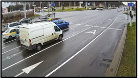 OV camera view of a van and other vehicles parked or stopped along a wide roadway with turn-lane arrow markings