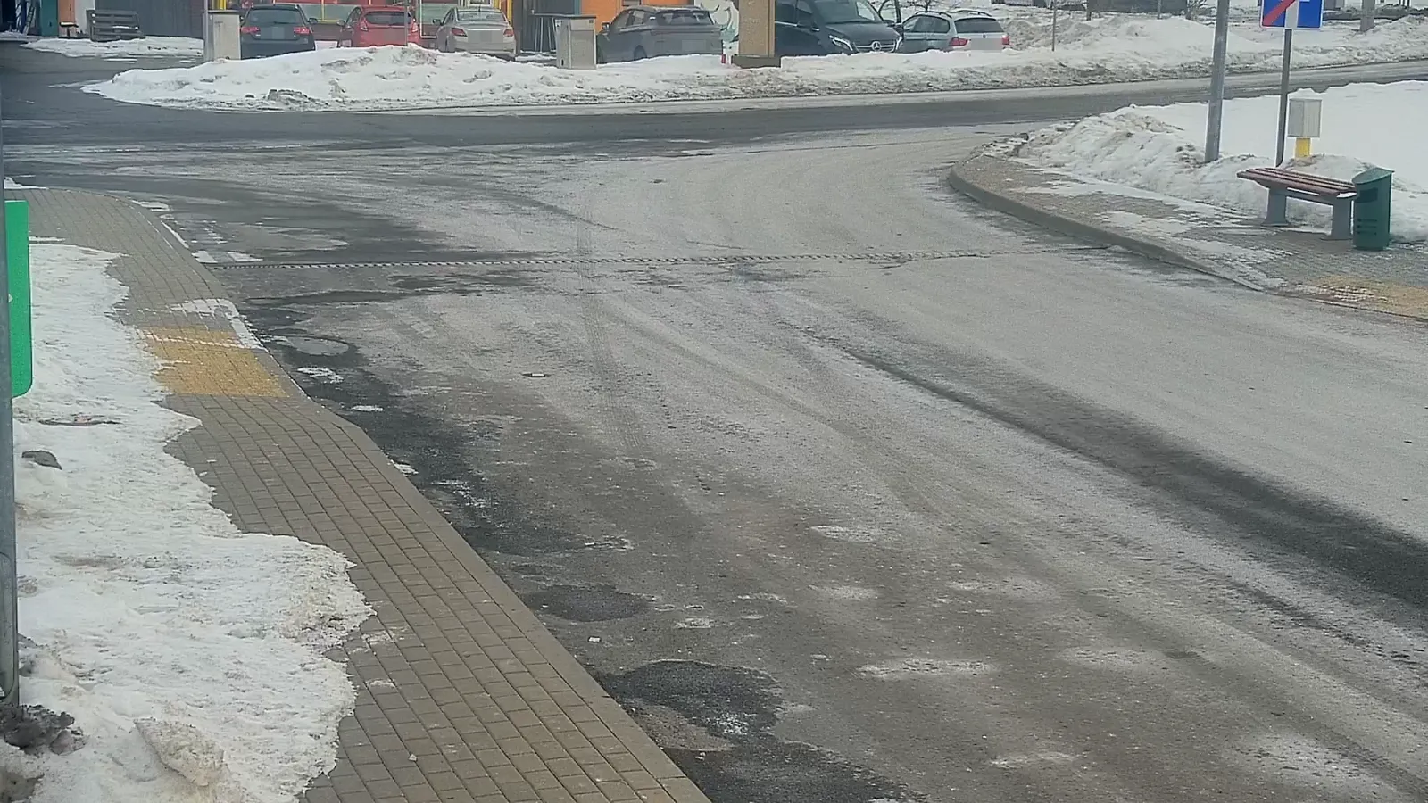 LPR camera view of a snowy intersection road curve with parked cars, a bus shelter, and no vehicles crossing