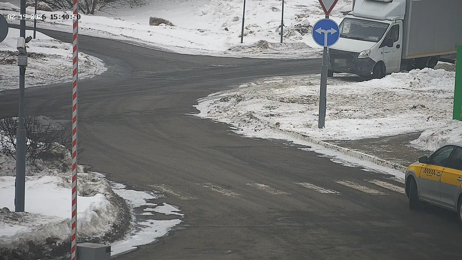 LPR camera view of a snowy road junction with a delivery van, a mandatory-direction sign, and a taxi approaching
