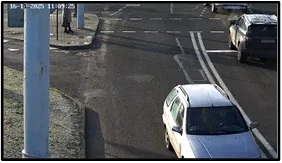 Exit LPR camera view of a sedan and other vehicles exiting the intersection past a pole-mounted camera housing