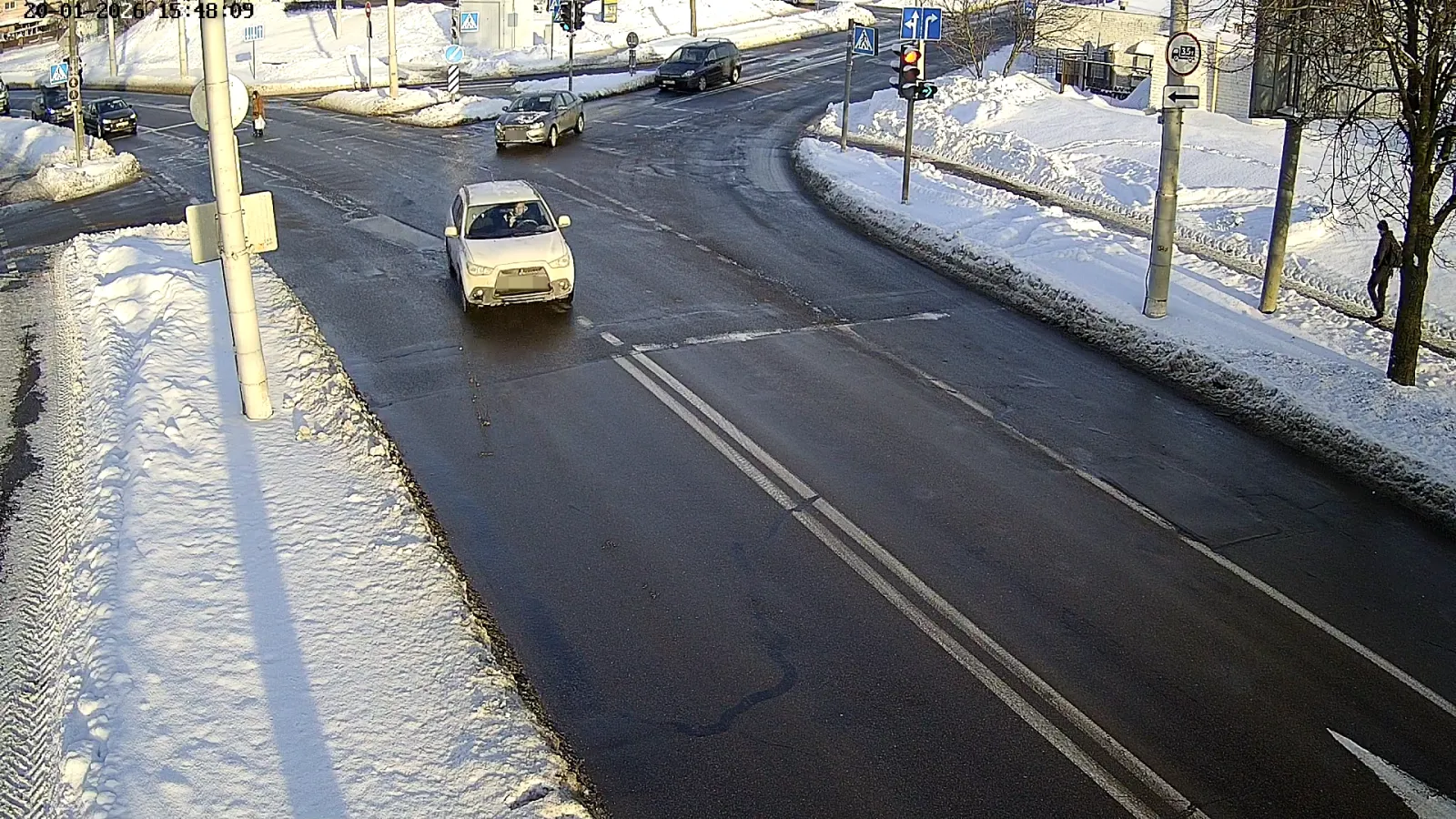 OV camera wide shot of a snowy road junction with traffic lights, road signs, and a car crossing the intersection