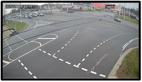 OV camera wide shot of an intersection approach with dashed guide lines and buildings visible in the background