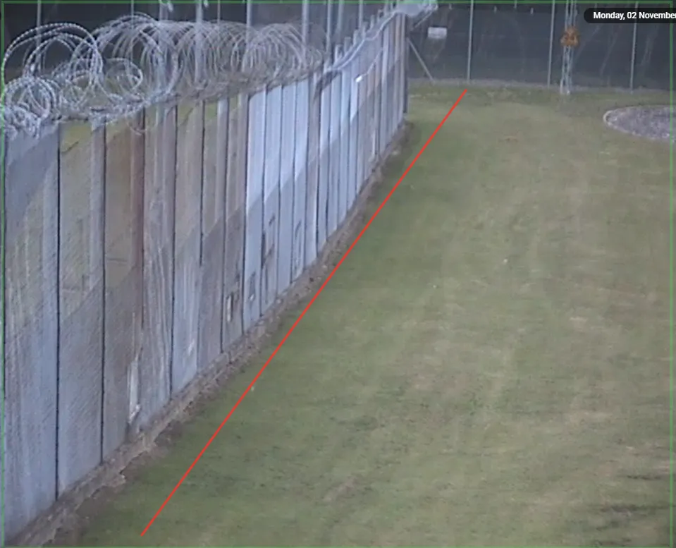 Camera view of a perimeter fence with a red line drawn across the frame to define the line-crossing rule